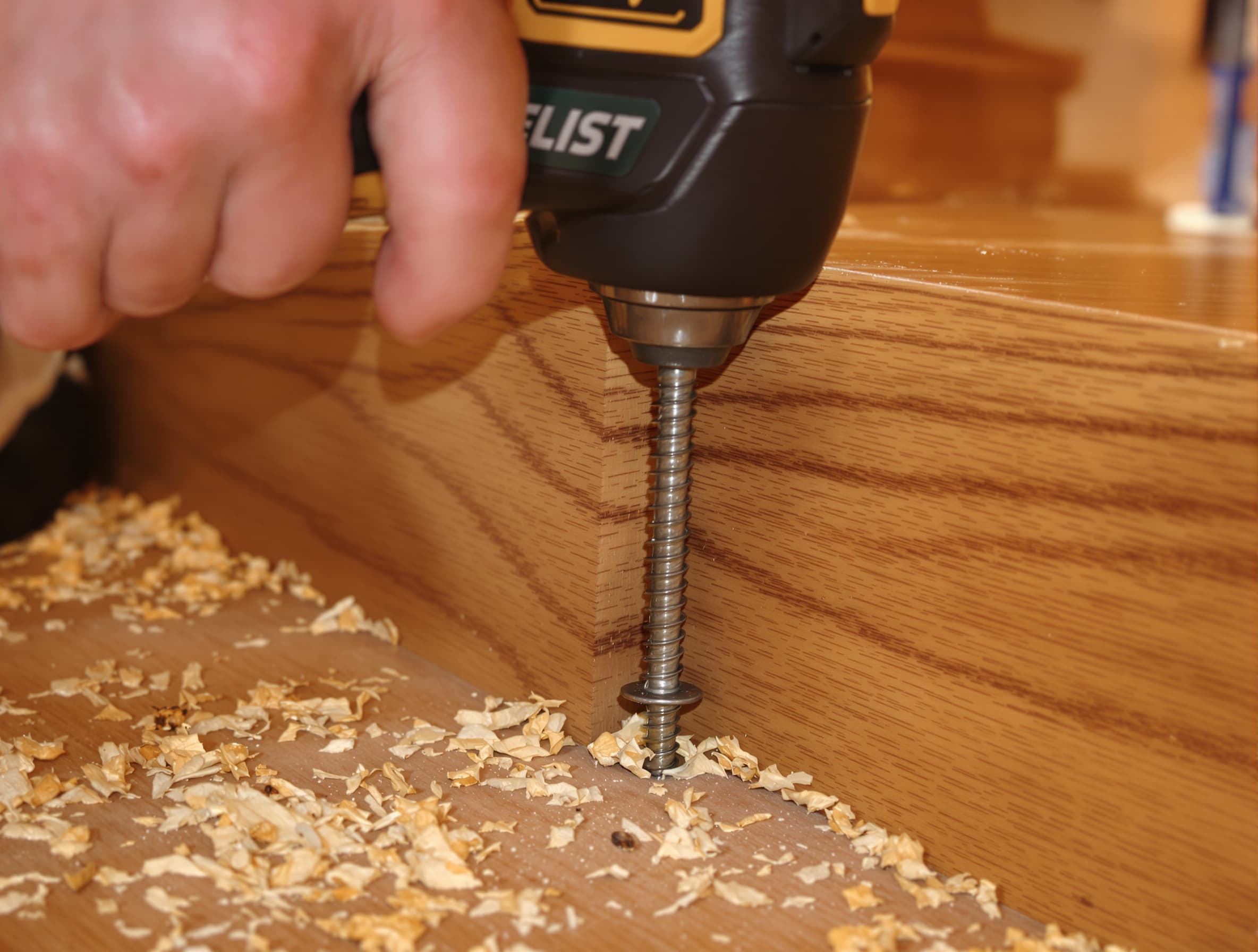 Close-up of a trim screw being driven into a squeaky stair tread and riser joint