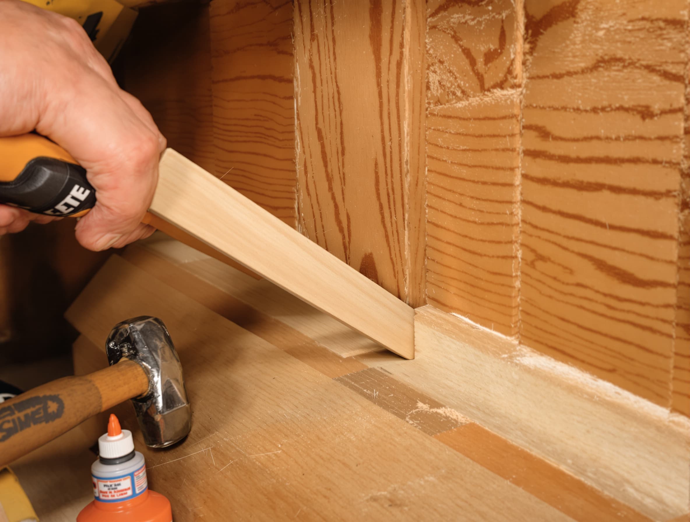Close-up of a wood shim being inserted into the gap under a squeaky stair tread